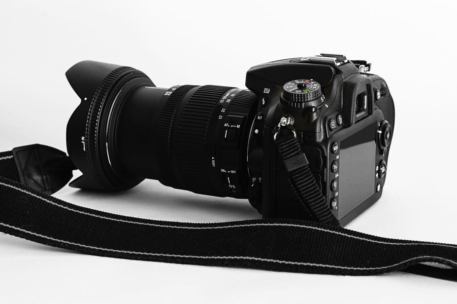 A DSLR camera with a zoom lens and strap, seen from the side
